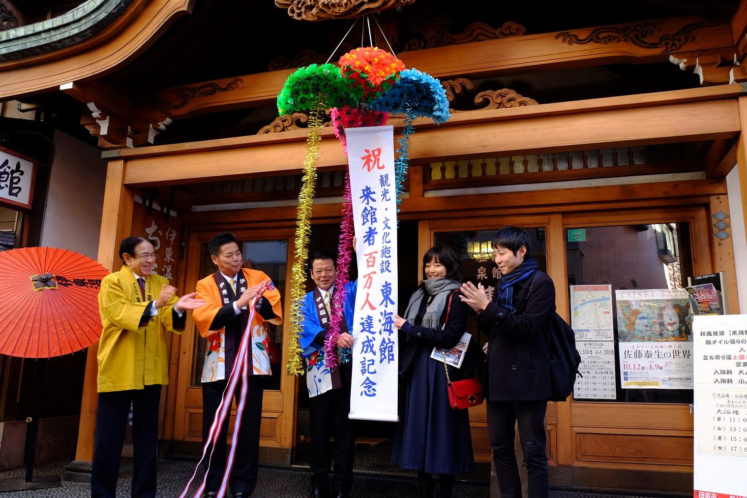 2017年12月9日東海館玄関前で開披したくす玉のタレ幕を節目の入館者と共に掴む市長の写真