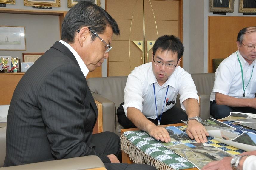 2018年8月7日 岩村明主事から写真を交えながら報告を受ける市長の写真