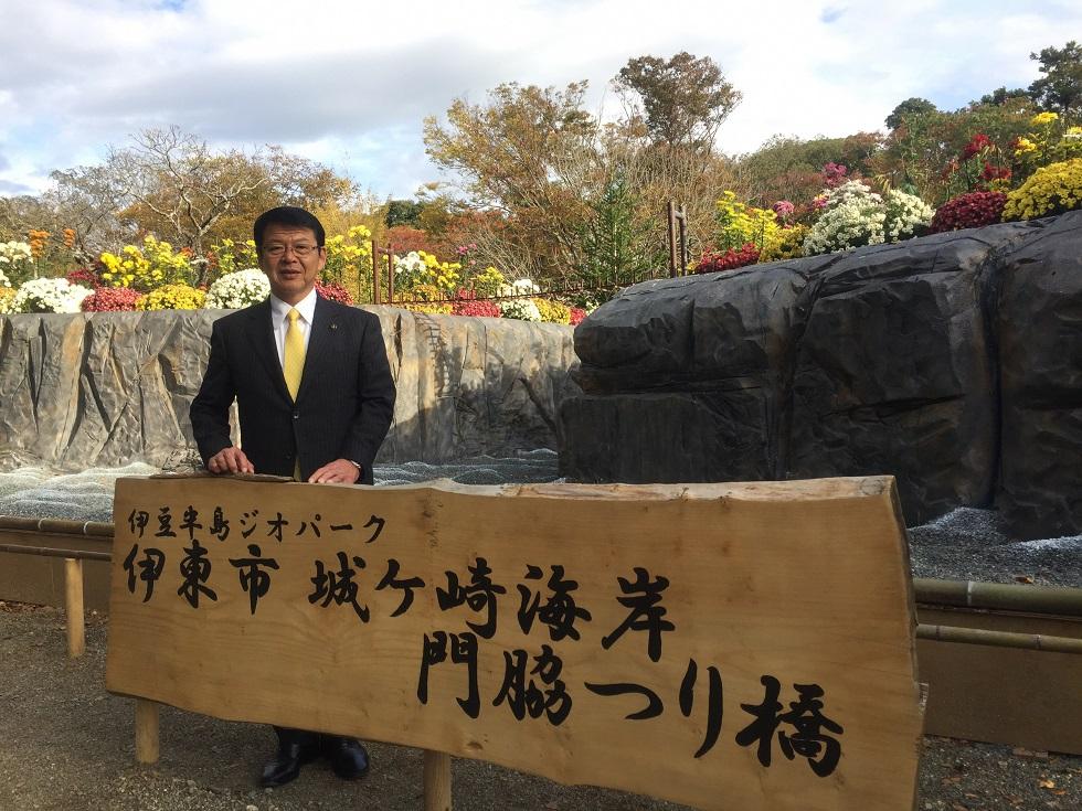 楽寿園菊祭りで伊豆半島ジオパークの看板の前でイベントPRをする伊東市長の写真