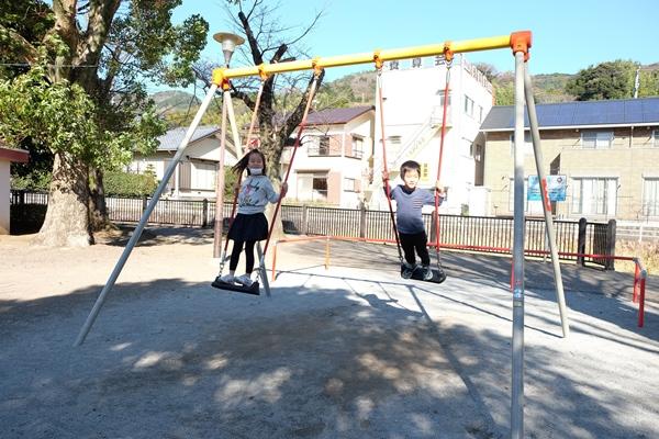 ブランコを立って漕ぐ女の子と男の子の写真