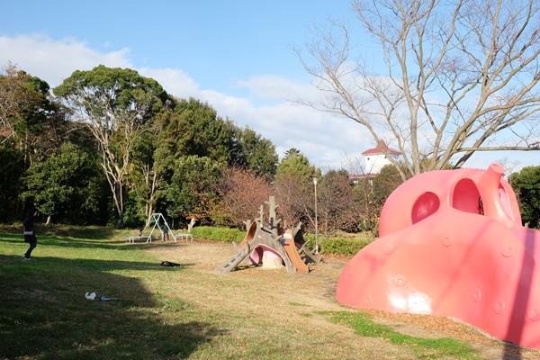 プレイスカルプチャーと滑り台とブランコと木々の写真