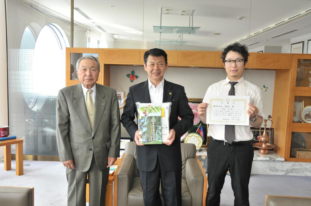 2017年7月3日受領証を掲げる株式会社植源さんと「木に関わる書籍」を掲げる市長の写真