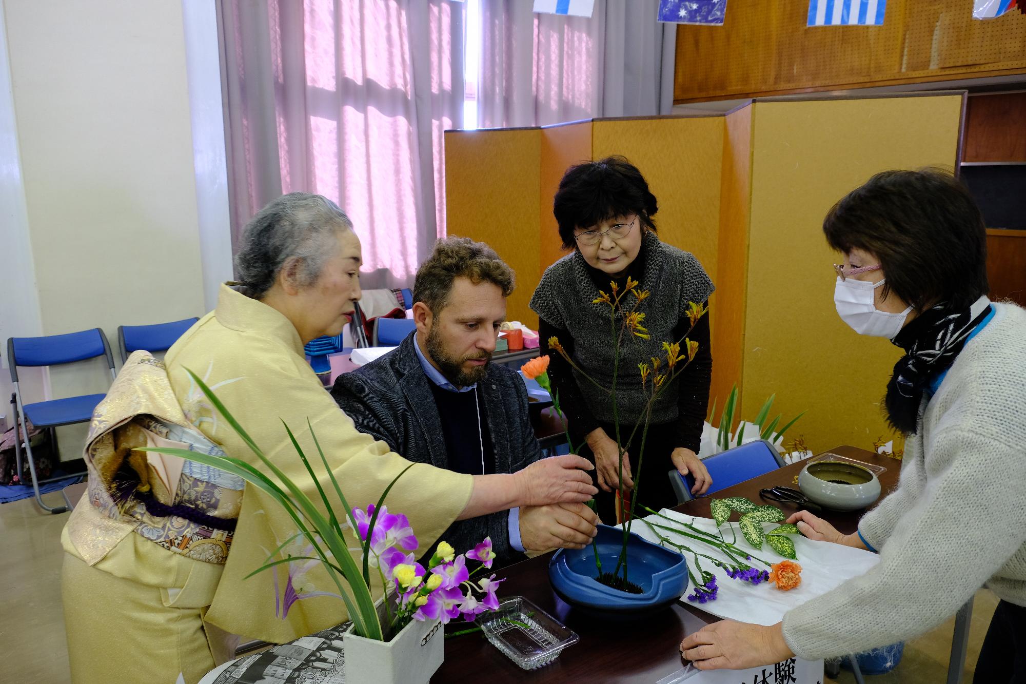 華道の先生からお花の生け方を教わっている外国人男性の写真
