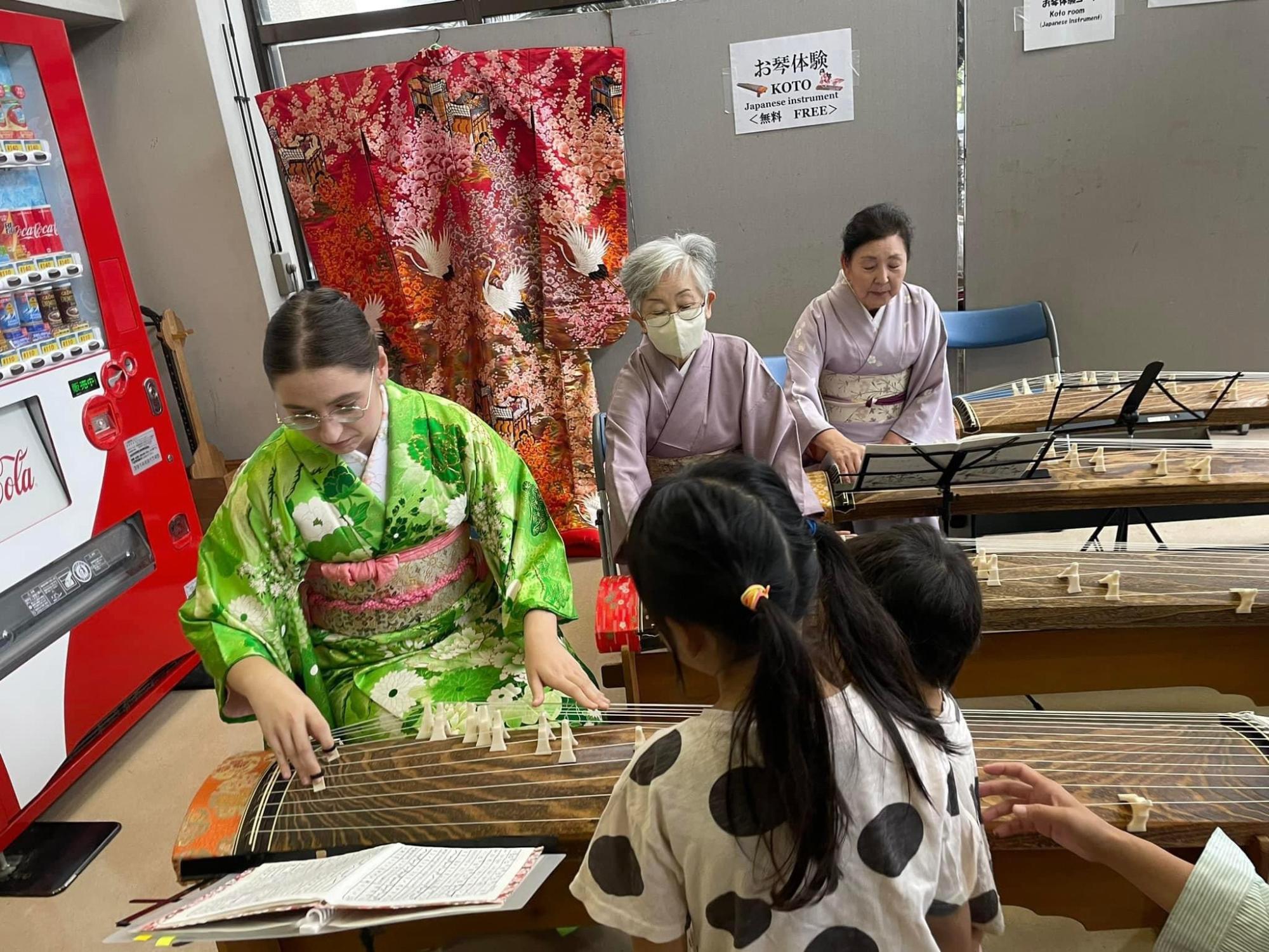 先生と一緒に琴を弾いている女性外国人とそれを見学している子どもたちの写真