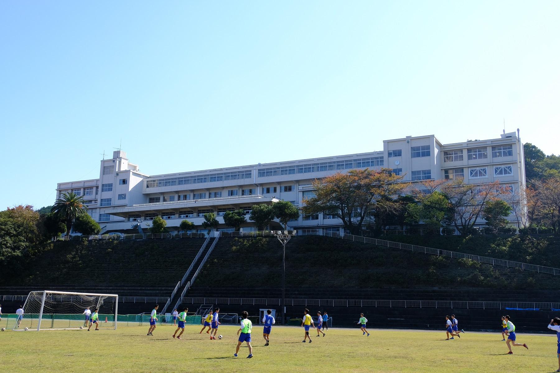 校舎とグラウンドでサッカーをする子供たちの写真