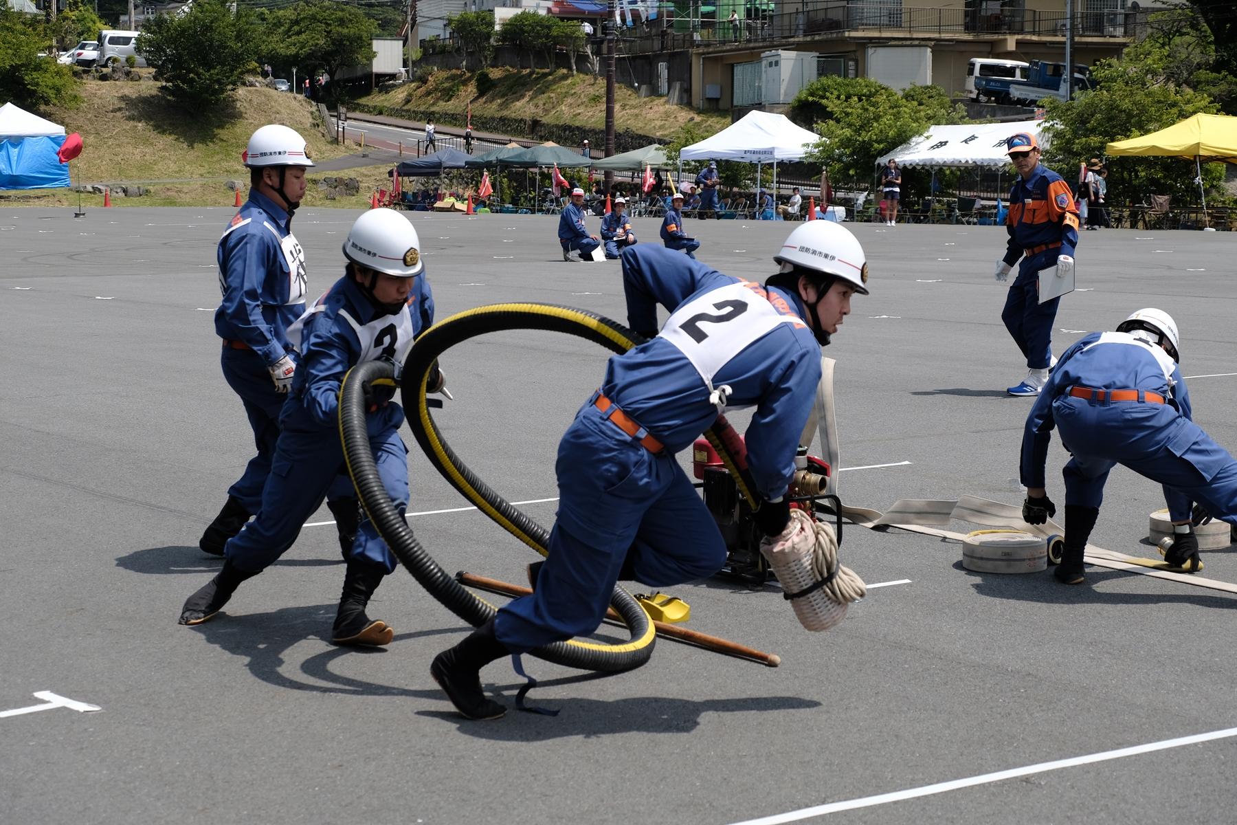 給水ホースを持って走る、競技中の伊東市消防団員の写真