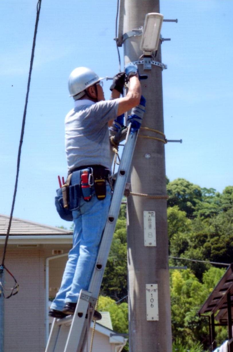 電信柱へかけた梯子に登り作業をする人の写真